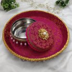 Decorative red and gold round bangles ceremony trays with white bead accents, featuring a smaller matching lidded container both adorned with intricate gold detailing and white bead accents. The vibrant red fabric features a subtle floral pattern