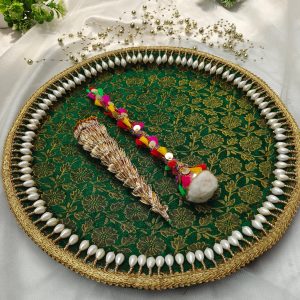 A decorated platter with a green and gold floral pattern, bordered with pearls, displaying a traditional Indian mehndi cone and a colorful decorative stick mehndi ceremony platter is perfect for wedding events, particularly the mehndi ceremony, where it can be used to present henna cones and other ceremonial items