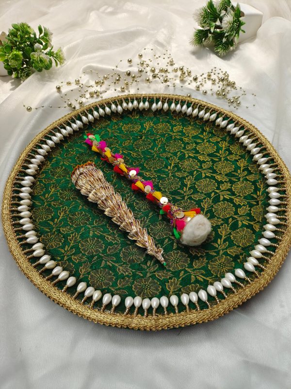 A decorated platter with a green and gold floral pattern, bordered with pearls, displaying a traditional Indian mehndi cone and a colorful decorative stick mehndi ceremony platter is perfect for wedding events, particularly the mehndi ceremony, where it can be used to present henna cones and other ceremonial items