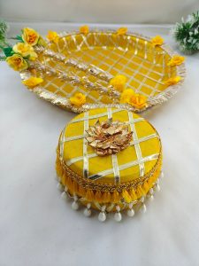 Charming yellow and gold steel platter with a lattice design, golden trims, and yellow flower accents, featuring a round box for Haldi and Henna ceremonies The centerpiece round steel box, with its pearl accents, is ideal for holding Haldi, Henna, or other special items wedding favor