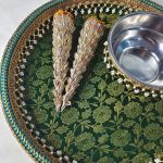 Wedding mehndi platter adorned with intricate designs, including two ornate cones and a stainless steel bowl, set on a green and gold floral background, perfect for wedding ceremonies