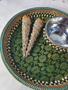 Wedding mehndi platter adorned with intricate designs, including two ornate cones and a stainless steel bowl, set on a green and gold floral background, perfect for wedding ceremonies
