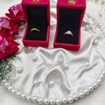 Ring ceremony platter with red velvet ring box, placed on a white satin cloth adorned with pearls. The setup includes red roses, greenery, and gold bead decorations, ideal for wedding jewelry presentations ring ceremony platter