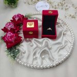 Beautiful wedding ring ceremony setup with a gold ring in a red velvet box on a pearl-trimmed satin cloth, enhanced by red roses and greenery attracting brides-to-be with its elegant presentation