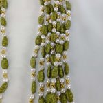 A pair of Welcome Milni Mala Moti Haar, adorned with green beads and golden pearls, laid on a white fabric, perfect for welcoming guests at weddings and Nikah ceremonies