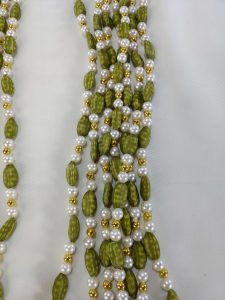 A pair of Welcome Milni Mala Moti Haar, adorned with green beads and golden pearls, laid on a white fabric, perfect for welcoming guests at weddings and Nikah ceremonies