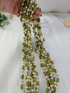 Elachi designed Welcome Milni Mala Moti Haar with green and gold beads and pearls, laid out on a white fabric, ideal for Nikah ceremonies and wedding traditions