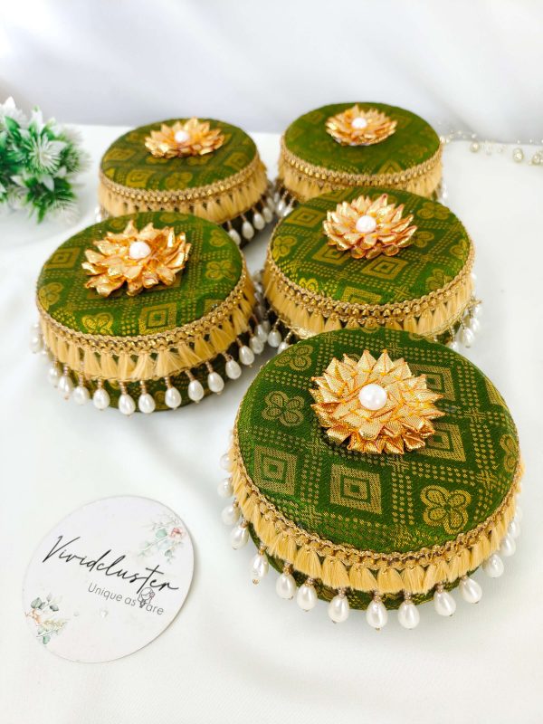 Set of green laddu boxes, each decorated with golden floral patterns and topped with a golden floral motif and pearl. The boxes feature golden lace and hanging white pearl beads, adding a touch of elegance for wedding celebrations