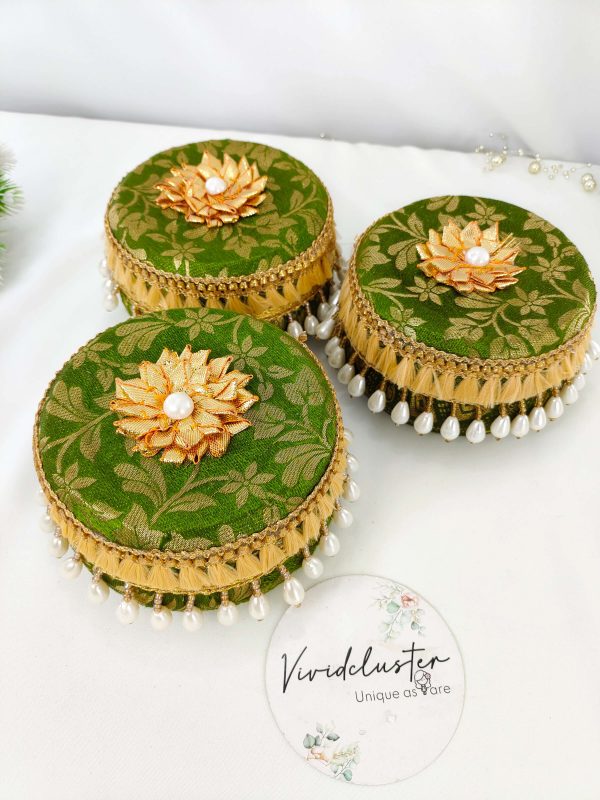Set of green laddu boxes, each decorated with golden floral patterns and topped with a golden floral motif and pearl. The boxes feature golden lace and hanging white pearl beads, adding a touch of elegance for wedding celebrations