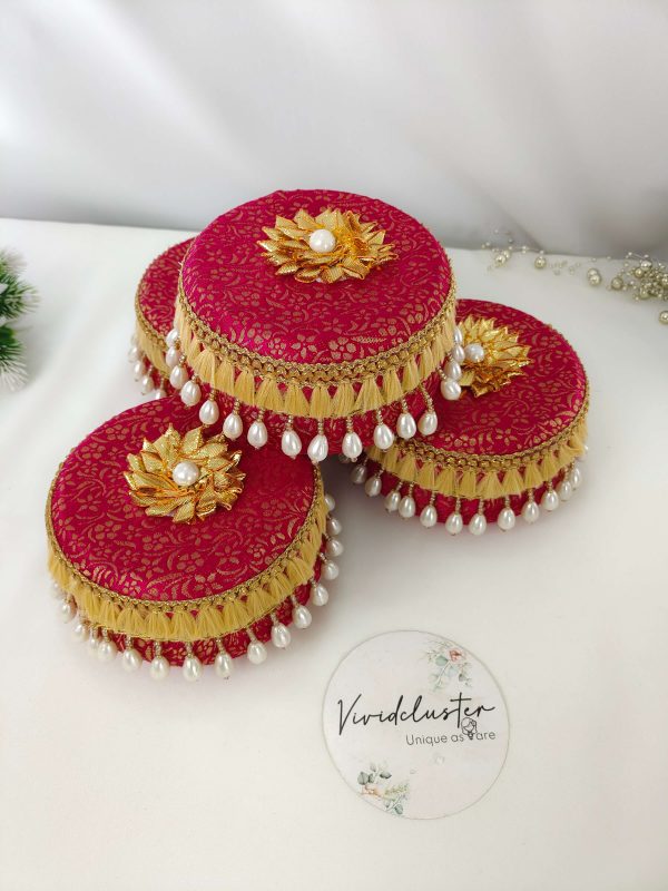 red round laddu boxes with intricate golden floral designs, golden floral motifs topped with pearls, and edges adorned with golden lace and white pearl beads, creating a look ideal for wedding favors bridesmaids gift