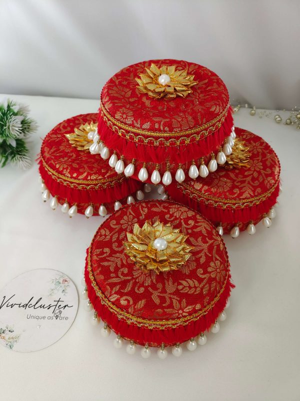 A set of fou red round laddu boxes, beautifully decorated with intricate golden floral patterns. Each box is topped with a golden floral motif and pearl, with edges adorned with golden lace and white pearl beads, showcasing elegant craftsmanship its a gift laddu box for Barati, Bridesmaids, Shagun Laddu Boxes