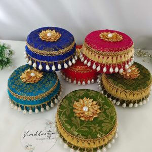 A set of four beautifully decorated round laddu boxes in vibrant blue fabric with intricate golden floral patterns Each box is adorned with a golden floral motif topped with a pearl its a gift laddu box for Barati, Bridesmaids, Shagun Laddu Boxes