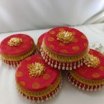 Decorative red laddu boxes with gold floral designs and pearl accents distributing traditional sweets like laddus, which are often served during the Haldi ceremony