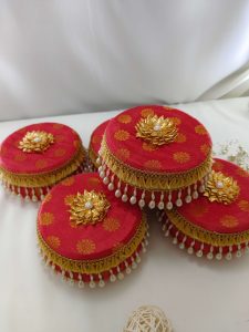Decorative red laddu boxes with gold floral designs and pearl accents distributing traditional sweets like laddus, which are often served during the Haldi ceremony
