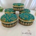 Vibrant teal, green, yellow, and white round shagun boxes with intricate gold detailing and pearl accents, perfect for wedding favors