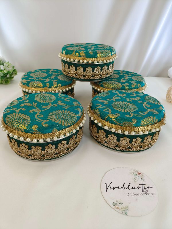 Vibrant teal, green, yellow, and white round shagun boxes with intricate gold detailing and pearl accents, perfect for wedding favors