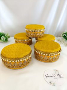 Stylish wedding laddu boxes with yellow and gold detailing and pearl accents in teal, green, yellow, and white, featuring a durable stainless steel interior