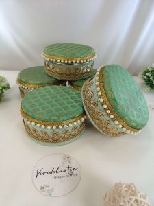 Decorative laddu shagun boxes in bright colors with elegant gold embroidery and pearls, showcasing their use for wedding and engagement ceremonies return gift