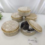 Round wedding shagun boxes with intricate gold embroidery and pearl accents in pink colors, one box opened to display its stainless steel interior for giveaway gifts