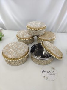 Round wedding shagun boxes with intricate gold embroidery and pearl accents in pink colors, one box opened to display its stainless steel interior for giveaway gifts