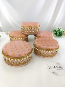 A set of colorful wedding laddu shagun boxes adorned with gold embroidery and pearls, showcasing their elegant design and stainless steel interior shagun boxes, a memorable return gift