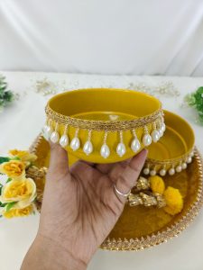 two elegant yellow bowls decorated with delicate pearl trim and complemented by intricate golden lace for holding the turmeric paste used in the Haldi ritual a perfect blend of tradition