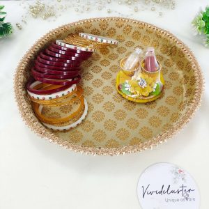 A gold decorative platter with intricate patterns, designed for a Bangle Chuda ceremony. The platter features a beautifully detailed border and a central logo that reads