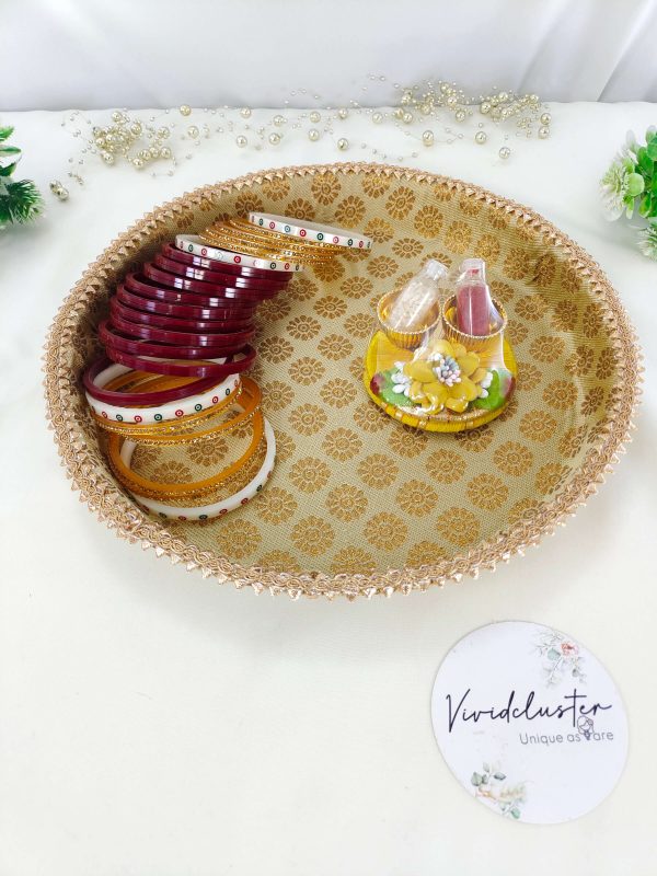 A gold decorative platter with intricate patterns, designed for a Bangle Chuda ceremony. The platter features a beautifully detailed border and a central logo that reads