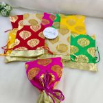 A vibrant collection of traditional tissue wedding potlis in various colors, designed with golden motifs, perfect for wedding favors.