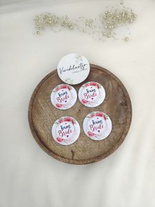 A round, pink, white brooch with the words bride side and a delicate flower design for the bride's side. Perfect for baraat day, nikah ceremonies, or as a unique wedding favor