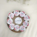 A round, pink, white brooch with the words bride side and a delicate flower design for the bride's side. Perfect for baraat day, nikah ceremonies, or as a unique wedding favor