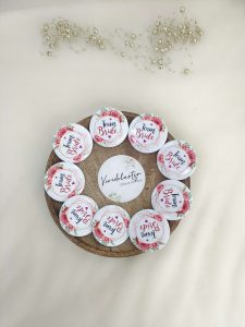 A round, pink, white brooch with the words bride side and a delicate flower design for the bride's side. Perfect for baraat day, nikah ceremonies, or as a unique wedding favor