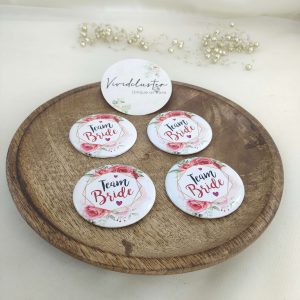 pink and white team bride brooch featuring the text team bride with a floral print accessory for bride's side members during wedding ceremonies, baraat day, or nikah events