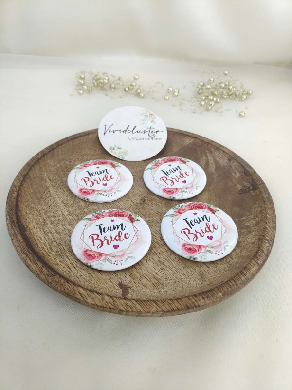 pink and white team bride brooch featuring the text team bride with a floral print accessory for bride's side members during wedding ceremonies, baraat day, or nikah events