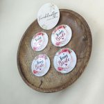 A round, pink, white brooch with the words bride side and a delicate flower design for the bride's side. Perfect for baraat day, nikah ceremonies, or as a unique wedding favor