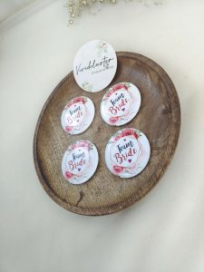 A round, pink, white brooch with the words bride side and a delicate flower design for the bride's side. Perfect for baraat day, nikah ceremonies, or as a unique wedding favor