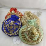 A collection of four designer Gota Patti Potli , Potlis in assorted colors adorned with intricate golden embroidery and pearl handles, perfect for wedding ceremonies.