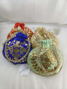 A collection of four designer Gota Patti Potli , Potlis in assorted colors adorned with intricate golden embroidery and pearl handles, perfect for wedding ceremonies.