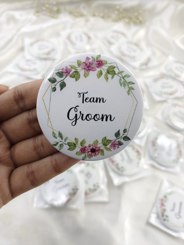 a round Team Groom Badges with "Team Groom" written in elegant black script. The brooch is adorned with pink and green floral designs at the top and bottom This wedding accessory is perfect for groomsmen at a nikah ceremony, adding a touch of elegance to their wedding attir
