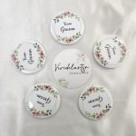 a round brooch with "Team Groom" written in elegant black script. The brooch is adorned with pink and green floral designs at the top and bottom This wedding accessory is perfect for groomsmen at a nikah ceremony, adding a touch of elegance to their wedding attir