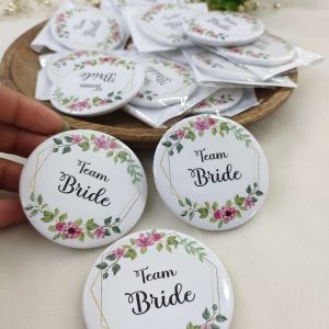 A round, pink, white Team Bride Brooches with the words bride side and a delicate flower design for the bride's side. Perfect for baraat day, nikah ceremonies, or as a unique wedding favor