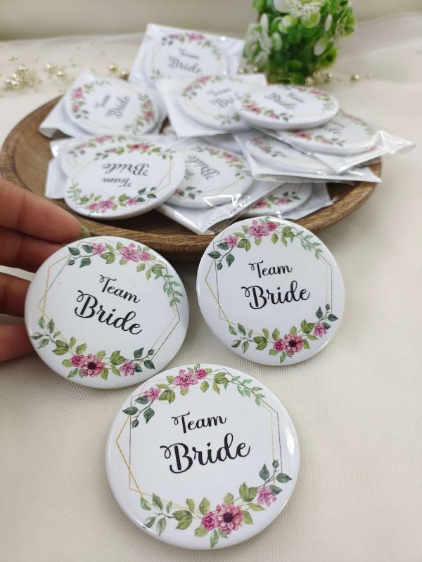 A round, pink, white Team Bride Brooches with the words bride side and a delicate flower design for the bride's side. Perfect for baraat day, nikah ceremonies, or as a unique wedding favor