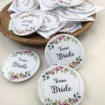 pink and white team bride brooch featuring the text team bride with a floral print accessory for bride's side members during wedding ceremonies, baraat day, or nikah events