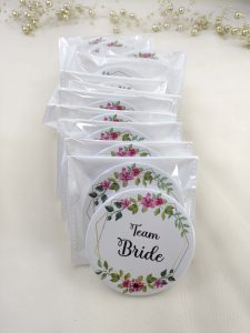 A round, pink, white brooch with the words bride side and a delicate flower design for the bride's side. Perfect for baraat day, nikah ceremonies, or as a unique wedding favor