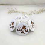 TEAM GROOM" brooches, white with brown text and a decorative top hat and mustache, Perfect for wedding attire accessories and baarati gifts.
