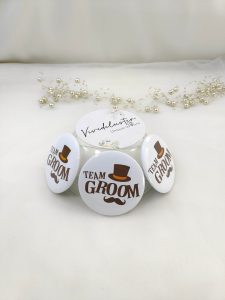 TEAM GROOM" brooches, white with brown text and a decorative top hat and mustache, Perfect for wedding attire accessories and baarati gifts.