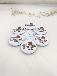 White circular pins with "TEAM GROOM" in bold brown font, accented by a brown top hat and mustache, Ideal for nikah ceremonies and wedding party accessories