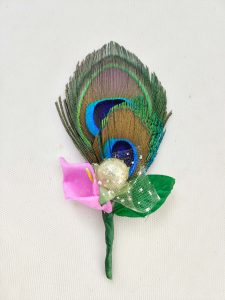 Wedding-themed brooch showcasing a colorful peacock feather, pink flower, and golden decoration, perfect for guests