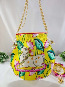 drawstring potli bag with a delightful cow illustration, set against a vivid yellow canvas with pink and green floral elements