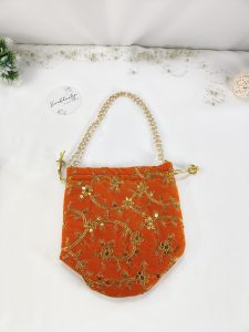 this embroidered potli bag features golden floral designs on rich orange fabric. Perfect for wedding ceremonies, bridal showers, or as a nikah gift. This potli bag serves as a beautiful wedding favor, bridesmaid gift, or a charming accessory for the bride